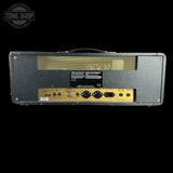 The rear view of a black guitar amplifier head with gold-colored input panel and gold mesh grille, shown against a solid black background with a Tone Shop watermark in the top left corner.