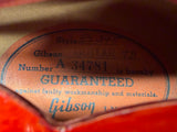 Close-up of a vintage Gibson guitar inner label with blue text on a tan background, partially framed by red and orange edges.