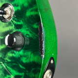 Close-up of a green electric guitar body showing the glossy flamed maple wood finish, control knobs, and a noticeable black scratch or wear mark on the side.