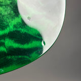Close-up of a curved green glass object with a glossy finish, showing a small droplet and a reflective white area against a neutral gray background.