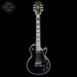 A black electric guitar with gold hardware and white binding, shown from the front against a solid black background. A 'TONE SHOP' watermark is visible in the top-left corner.
