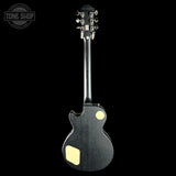 Black electric guitar with gold hardware on a black background, featuring 'Tone Shop' logo.