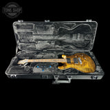 An electric guitar with a natural flame maple body and a light wood neck, displayed inside an open black hard case with gray velvet lining. A Tone Shop watermark is visible in the top left corner.