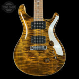 A close-up of an electric guitar body with a natural figured wood flamed finish, black humbucker pickups, and a white pickguard, shown against a solid black background with a Tone Shop watermark in the top left corner.