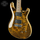A close-up of an electric guitar body with a natural figured maple top and a dark brown flame finish, featuring black humbucker pickups and chrome hardware, set against a solid black background.