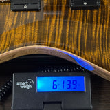 Close-up of an electric guitar body with a glossy brown wood finish being weighed on a black Smart Weigh scale displaying 61.39 kg.