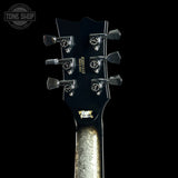 Close-up of a guitar headstock with tuning pegs on a black background, featuring the 'Tone Shop' logo.