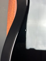 Close-up of a glossy black curved surface with a small white speckle and reflections, partially showing a brown wood-grain area below.