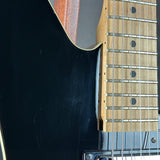 Close-up detail of an electric guitar showing the black body, maple fretboard, silver metal frets, and strings.