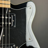 Close-up of a black electric guitar body with a white pickguard, chrome hardware, and part of the neck on a dark gray background.
