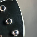 Close-up of a glossy black guitar body with three chrome control knobs against a neutral gray background.