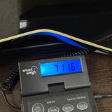 A close-up of a digital smart weigh scale displaying '7116' on its blue backlit screen, resting on a dark wooden surface with a black tray or mat underneath.