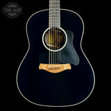 A close-up studio shot of the front of a dark acoustic guitar against a black background, showing the glossy black body, white binding, sound hole, pickguard, and natural wood bridge. A Tone Shop watermark is visible in the upper left corner.