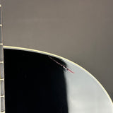 Close-up of a glossy black guitar body edge with a visible scratch or scuff on the reflective surface, against a dark gray background.