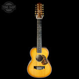 A 12-string acoustic guitar with a natural sunburst finish, shown vertically against a solid black background. A Tone Shop watermark is visible in the top-left corner.