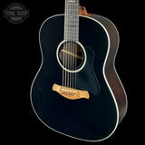 A black acoustic guitar with a glossy black finish, white binding, and a natural wood bridge, shown against a solid black background. A Tone Shop watermark is visible in the top-left corner.