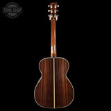 Acoustic guitar with a dark wood finish on a black background, featuring the Tone Shop logo.
