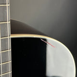 Close-up of the side edge of a black acoustic guitar body with a gold-toned edge trim and a visible red scratch on the glossy finish, next to the fretboard.
