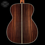 Back view of a wooden acoustic guitar with a visible brand logo in the corner.