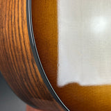 Close-up detail of a guitar body showing the glossy brown wood grain, a black binding edge, and a white fabric or felt overlay.