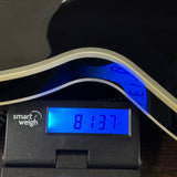 A close-up of a black digital smart weigh scale with a blue backlit display showing 8 lbs 13.7 oz, with a curved white object resting above it on the scale platform.