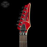 Close-up of an electric guitar headstock and upper neck against a black background, featuring a bright red flared headstock with a natural wood edge, chrome tuning hardware, and a dark fretboard. A Tone Shop watermark is visible in the top-left corner.