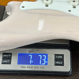 A close-up of a glossy off-white guitar body resting on a digital scale displaying 7.73 lbs.