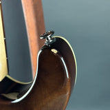 Close-up detail of an electric guitar body showing the glossy dark brown finish, cream edge trim, and a silver tuning peg against a dark gray background.