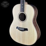 An acoustic guitar with a natural wood top and dark wood sides, shown against a solid black background. A Tone Shop watermark is visible in the top-left corner.