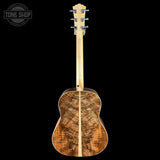 A back view of an acoustic guitar with a highly figured wood body and a natural maple neck, shown against a solid black background with a Tone Shop logo in the top-left corner.