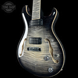 A close-up of an electric guitar body with a black and brown flame maple finish, featuring gold-toned hardware and a white binding edge, shown against a black background with a Tone Shop watermark.