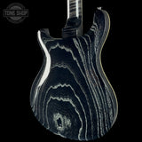 Close-up of the back of an electric guitar showing a glossy black finish with dramatic white and gray wood grain patterns, set against a solid black background with a Tone Shop watermark in the top-left corner.