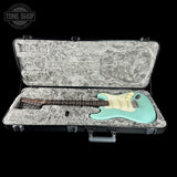 A mint green electric guitar with a white pickguard resting inside an open black hard case with a gray velvet-lined interior, shown against a solid black background.