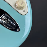 Close-up of a light blue electric guitar body showing part of the cream tone control dial, chrome hardware, and a dark background.