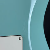 Close-up of a glossy light blue curved surface with a small portion of a white rectangular object visible in the lower left corner.