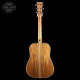 The back of a wooden acoustic guitar, showing the rich wood grain on the soundboard and neck, set against a solid black background with a Tone Shop logo in the top-left corner.