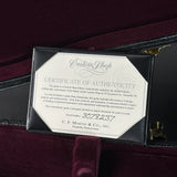 A close-up of a Martin Custom Shop Certificate of Authenticity insert displayed inside an open black presentation case lined with deep burgundy velvet. The certificate is octagonal with a white background and black text, featuring the Custom Shop logo and C.