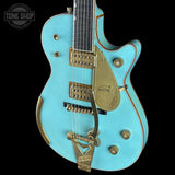Turquoise electric guitar with gold hardware on a black background, featuring 'Tone Shop' logo.