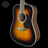 A classic acoustic guitar with a dark brown sunburst finish, shown from a three-quarters angle against a solid black background. A Tone Shop watermark is visible in the top-left corner.
