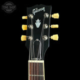 Close-up of a Gibson electric guitar headstock with six yellow tuning pegs, silver tuning keys, and a black faceplate on a black background.