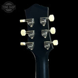 Close-up of a guitar headstock with six silver tuning pegs and cream-colored tuning keys on a black background. A Tone Shop watermark is visible in the top left corner.