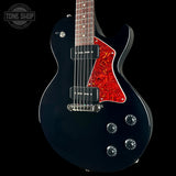 A black electric guitar with a vibrant red maple pickguard and a dark wood fretboard, shown against a solid black background with a Tone Shop watermark in the top left corner.