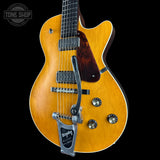 A Bigshot electric guitar with a natural sunburst finish, featuring a dark wood pickguard, chrome hardware, and a silver tremolo tailpiece, shown against a solid black background.