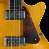 Close-up of a six-string electric guitar body showing the sunburst maple top, dark brown tortoiseshell pickguard, chrome hardware, and strings against a black background.