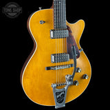 A close-up of a Les Paul Custom electric guitar with a natural maple top, dark brown sides, and chrome hardware, shown against a solid black background with a Tone Shop watermark in the top left corner.