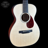 An acoustic guitar with a natural wood top, dark reddish-brown sides, and a dark red pickguard, shown against a solid black background with a Tone Shop watermark in the top-left corner.