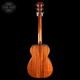 The back of a wooden acoustic guitar, showcasing a rich mahogany wood grain finish, set against a solid black background with a Tone Shop watermark in the top left corner.