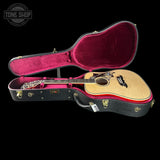 A Taylor acoustic guitar resting inside an open black hard case with a bright pink velvet interior, shown against a solid black background. A Tone Shop watermark is visible in the top-left corner.