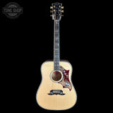 A Taylor acoustic guitar with a natural wood body, black headstock, and a decorative red and gold pickguard, shown against a solid black background with a Tone Shop watermark in the top left corner.