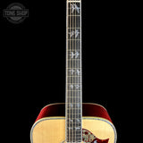 Close-up of an acoustic guitar neck and lower body against a black background, showing a natural wood fretboard with silver bird inlays and a red body interior. A Tone Shop watermark is visible in the top left corner.